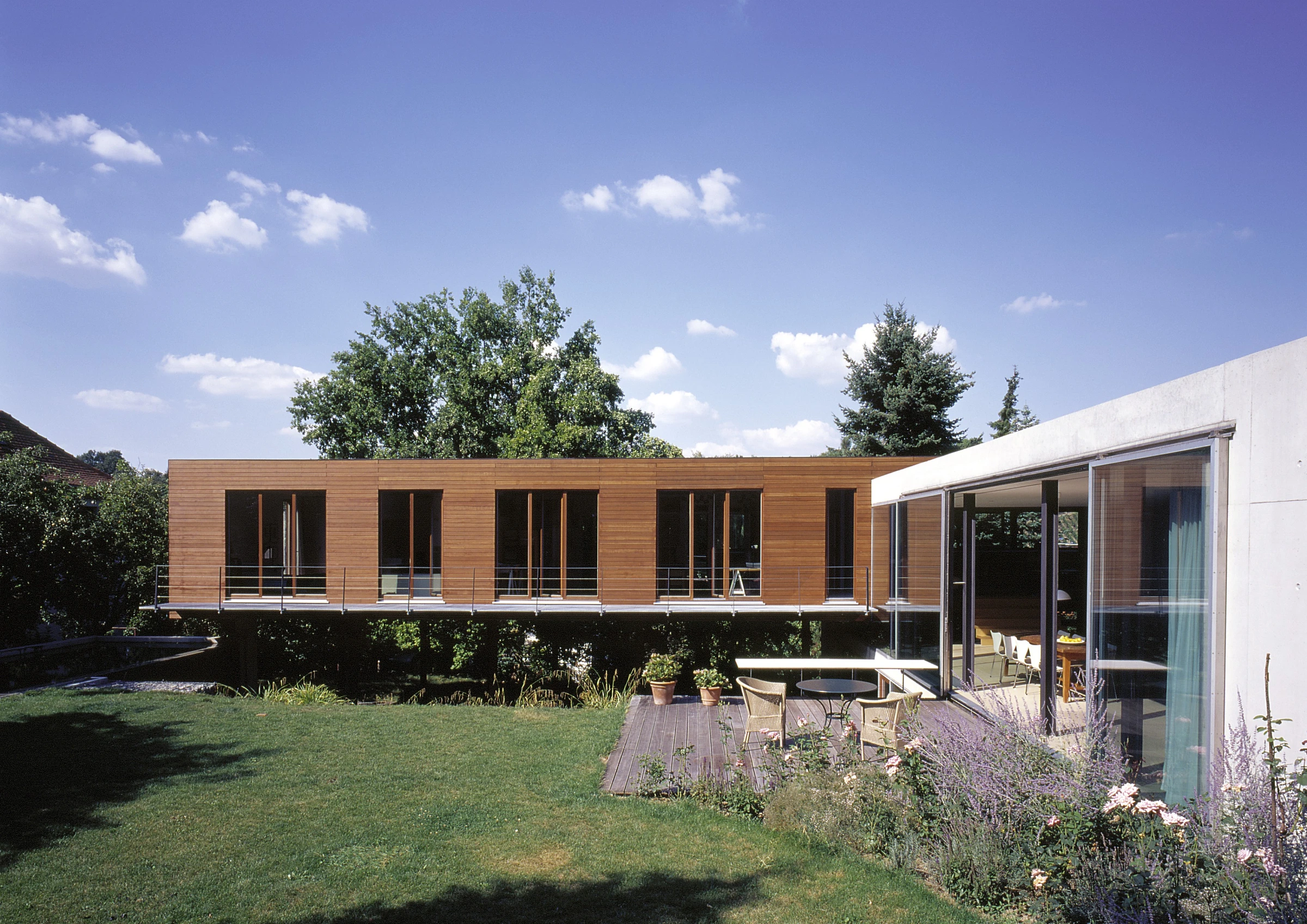 Blick auf einen aufgeständerten Gebäudeflügel, Holzfassade mit angrenzendem Pool