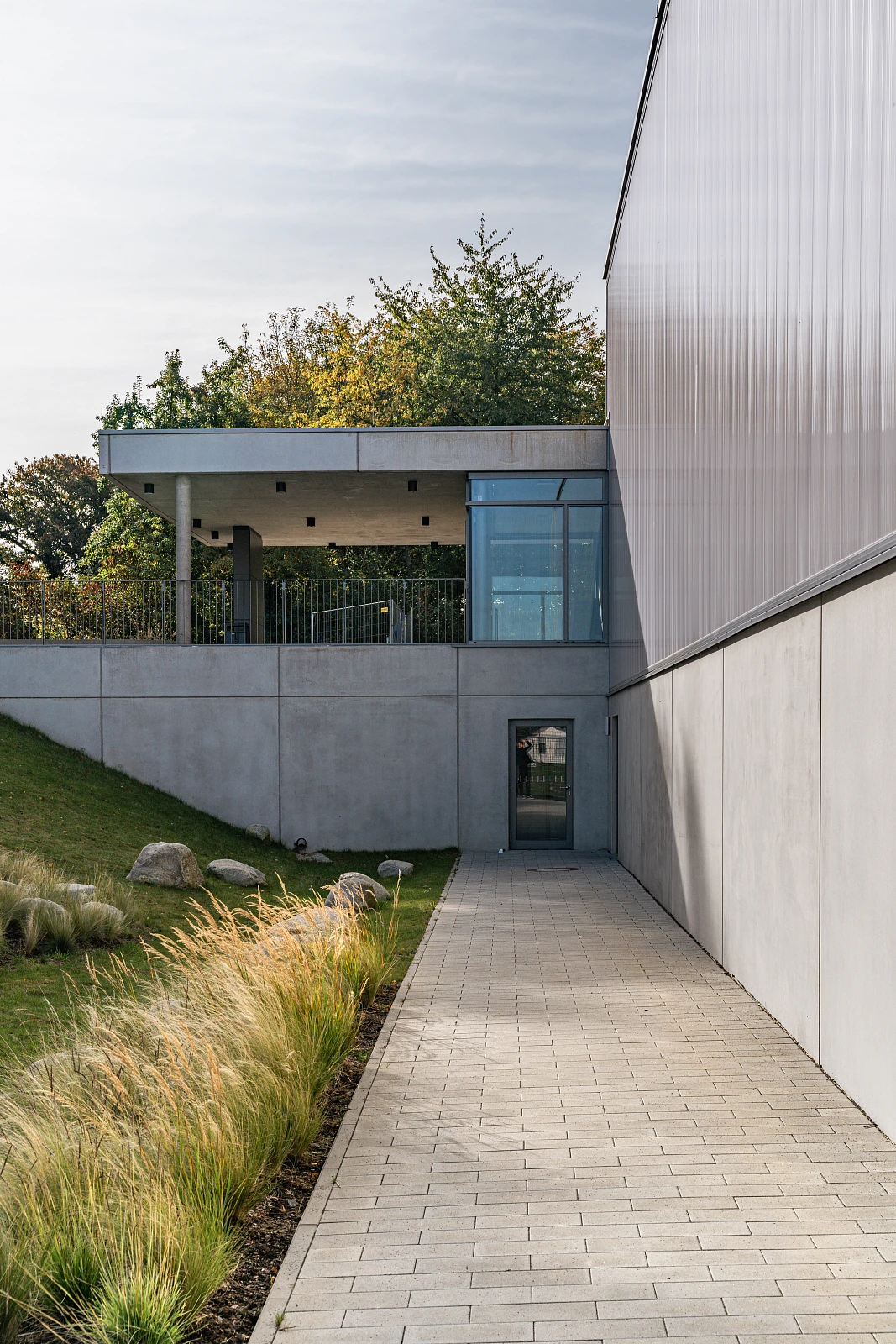 Dreifachsporthalle, Übergang zwischen verschiedenen Geländehöhen, Beton und Polycarbonat als Fassadenmaterial