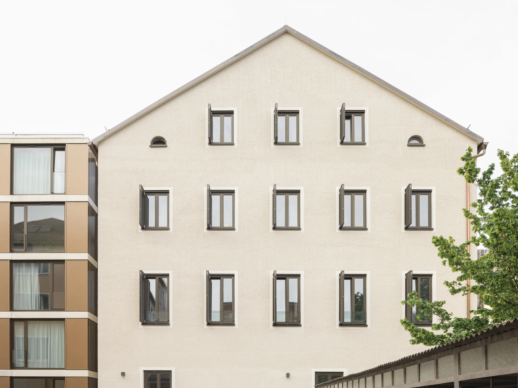 Studierendenwohnheim Ansicht Bestandgebäude mit Satteldach, Fensterläden aus Metall, Übergang zum Neubau